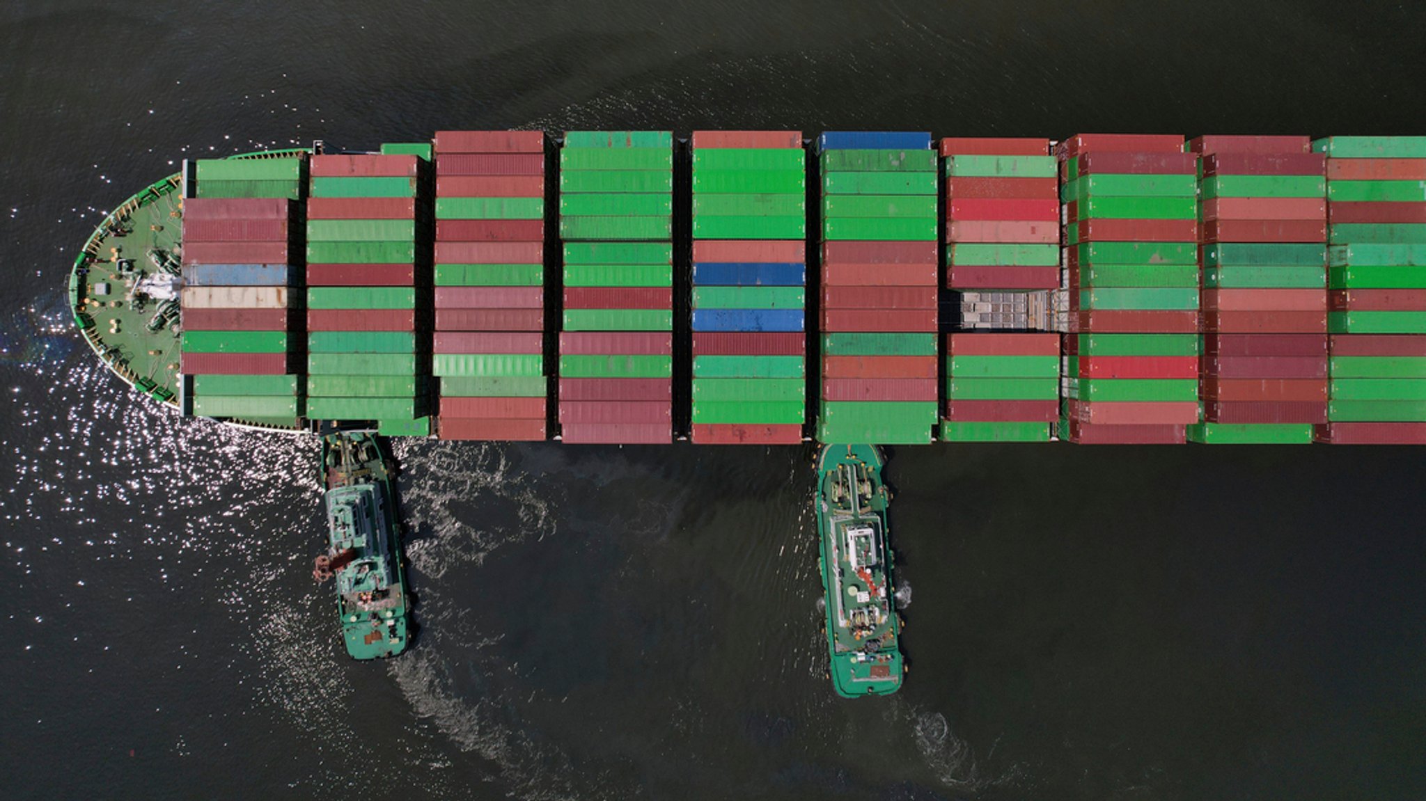 Schlepper helfen einem Containerschiff, das sich auf das Anlegen in einem Containerterminal vorbereitet (Symbolbild) 