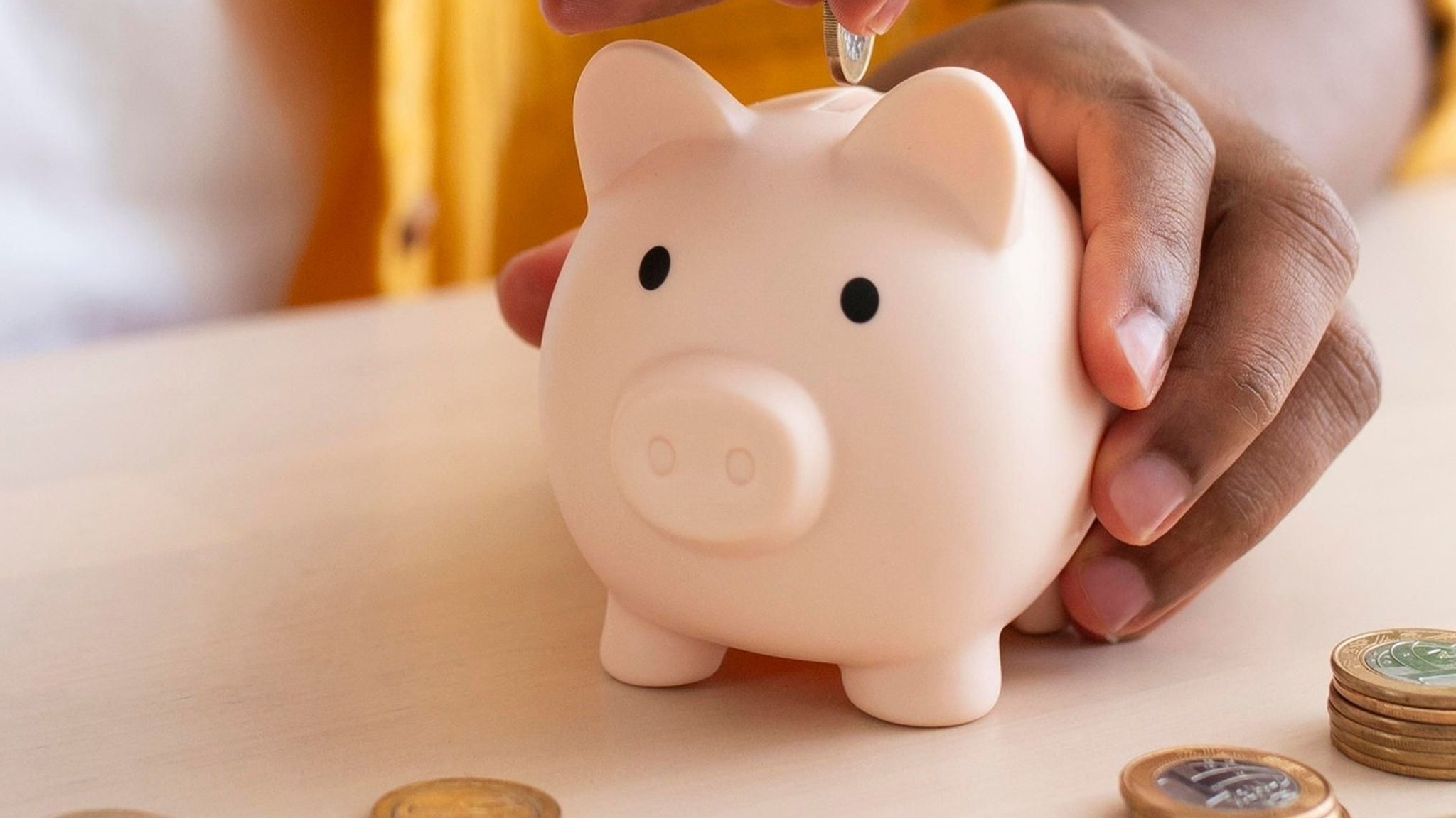Eine Hand steckt Geldstücke in ein Sparschwein