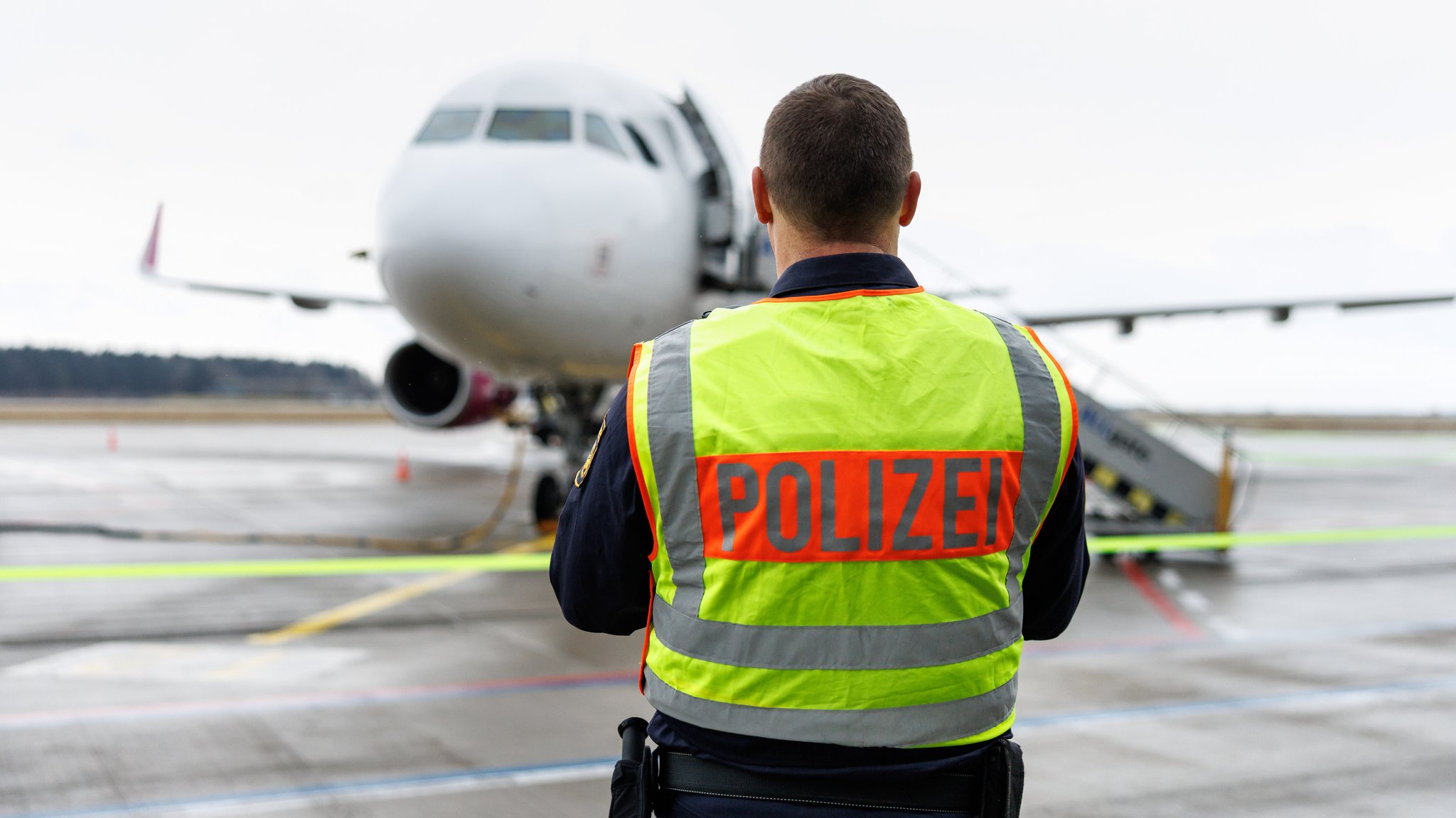 Ein Polizist mit einer Warnweste steht vor einem Flugzeug. 