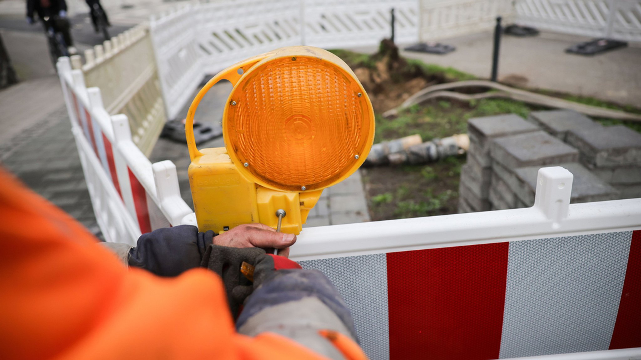 Ein Arbeiter sichert eine Baustelle mit Warnlampen am Absperrzaun (Symbolbild) | Bild: Christian Charisius/dpa/dpa-Bildfunk Ein Arbeiter sichert eine Baustelle mit Warnlampen am Absperrzaun (Symbolbild)